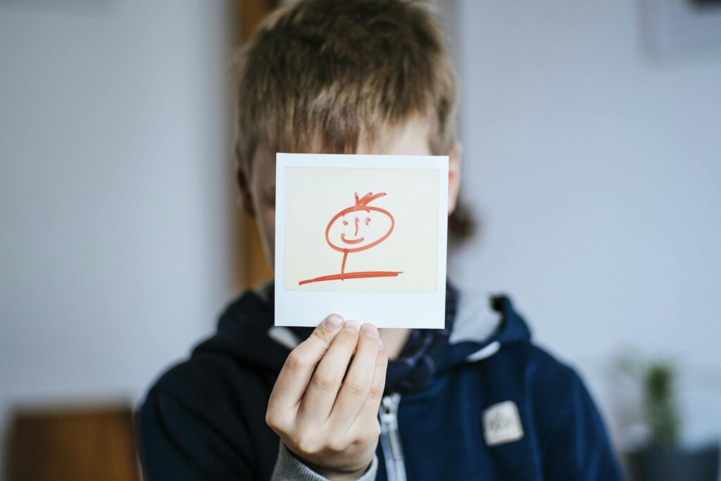 A child holding a hand-drawn stick figure portrait indoors.