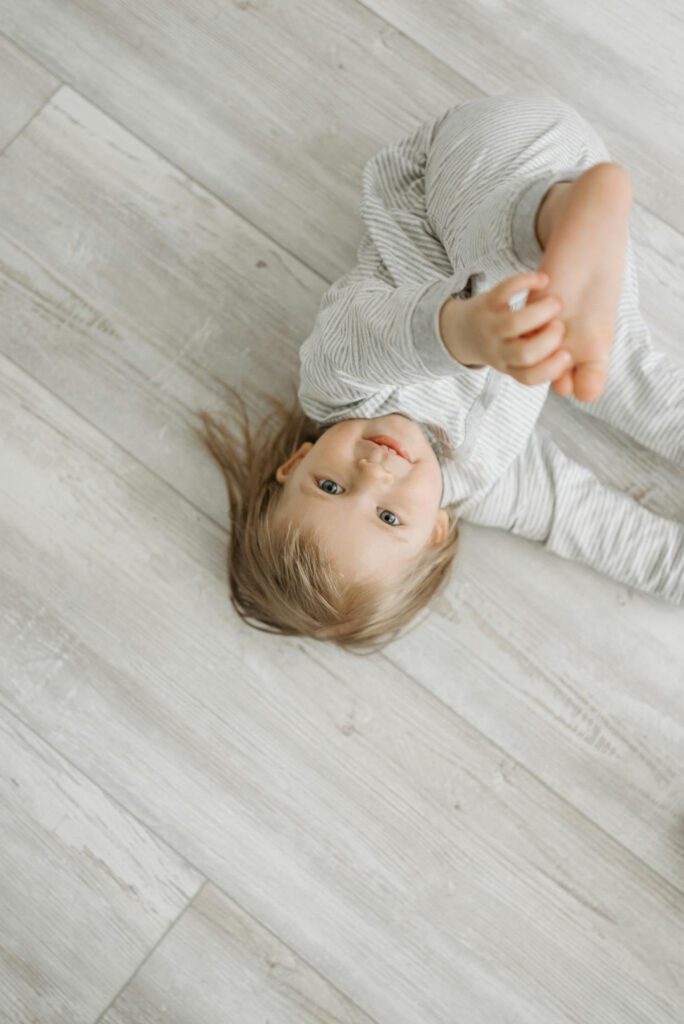 A cute baby girl in a striped outfit joyfully playing on a wooden floor, showcasing her playful spirit.