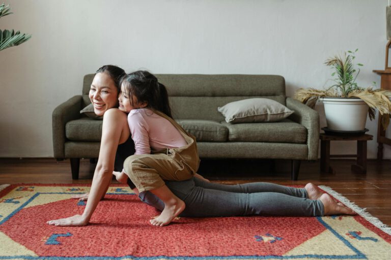 A joyful mother practicing yoga with her daughter on a colorful rug indoors.