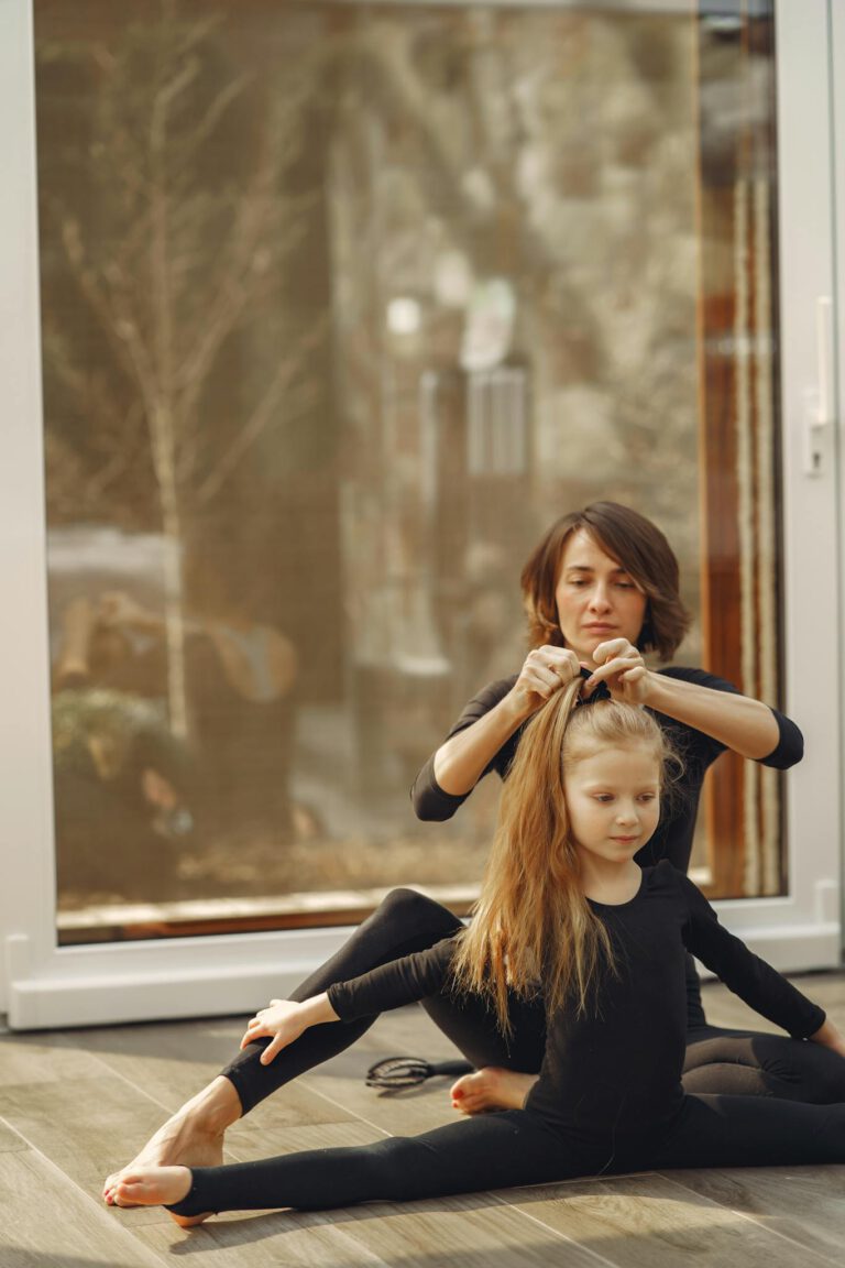 A mother helps her daughter stretch and fix her hair during a home workout session.